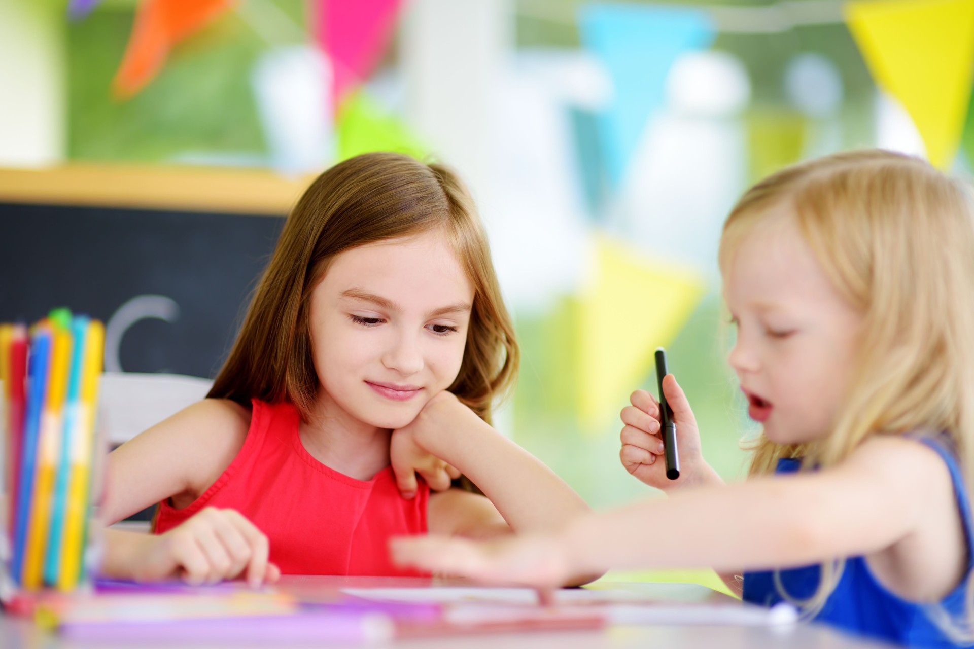 Two cute little sisters drawing with colorful pencils at a daycare. Creative kids painting together.