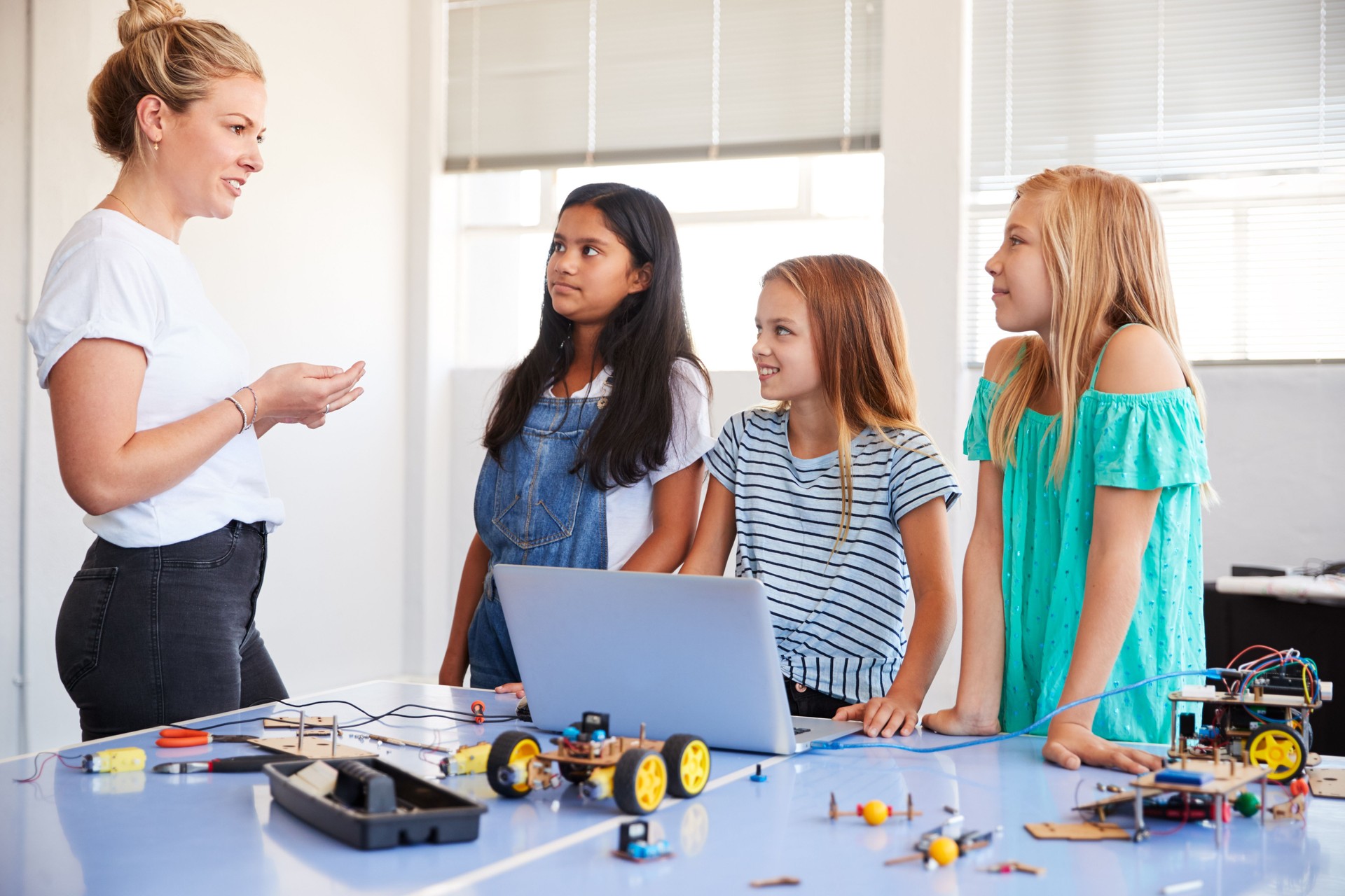 Three Female Students With Teacher Building Robot Vehicle In After School Computer Coding Class