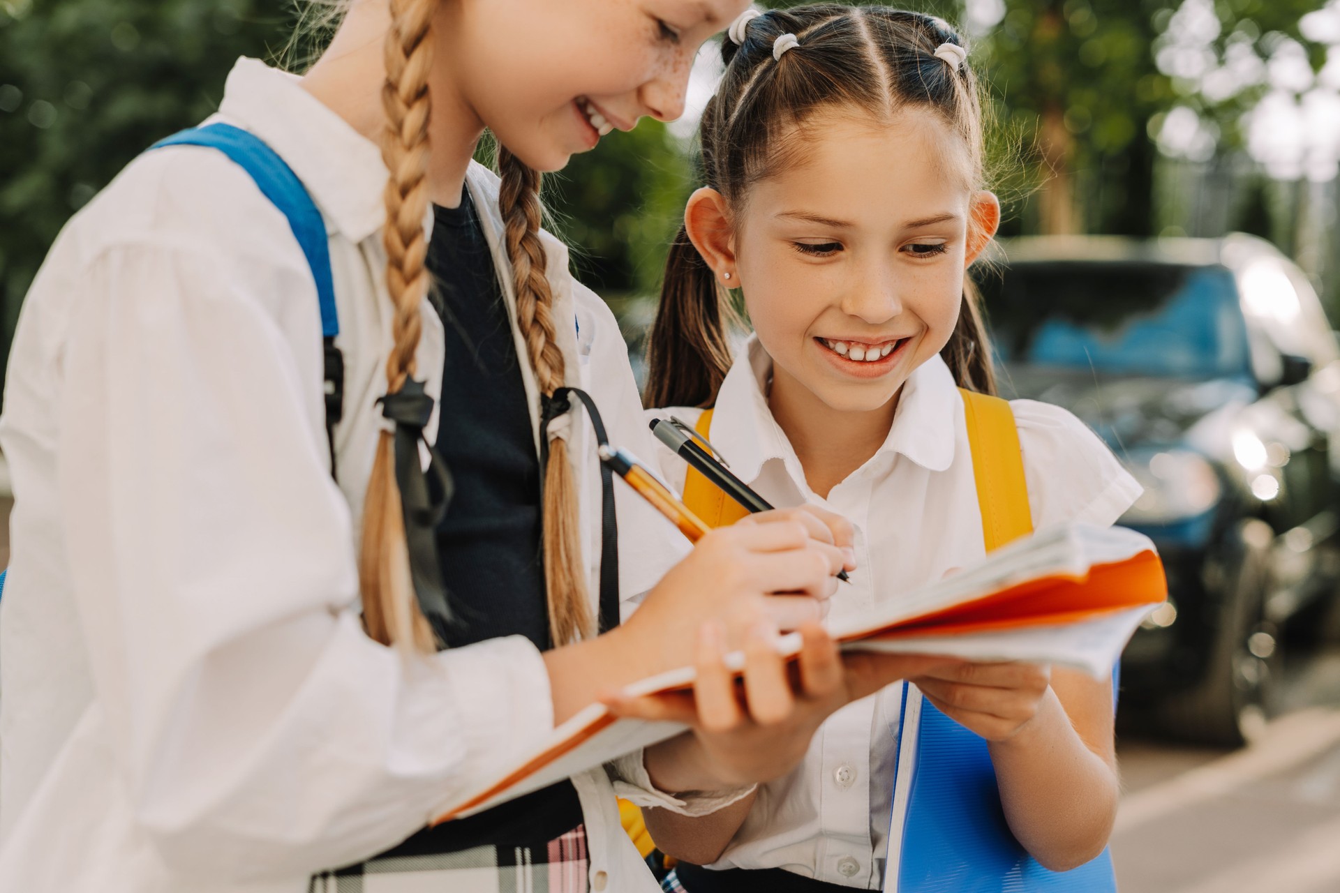 Two smiling schoolgirls sharing notes outdoors after school